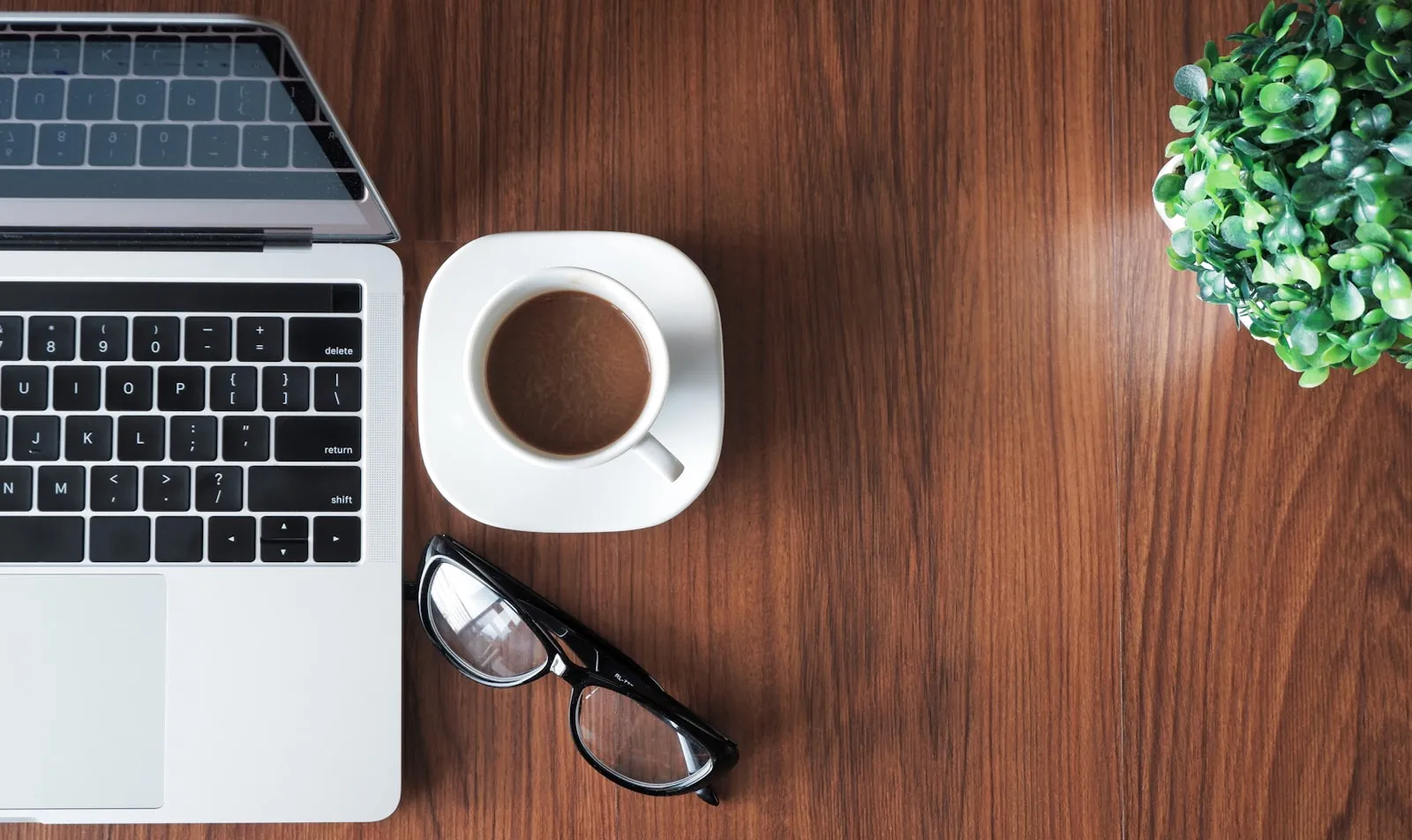 A tidy desk from above with a laptop, coffee and glasses