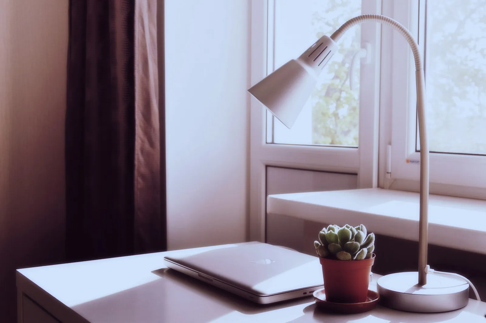 A calm, tidy desk with a closed laptop by a window